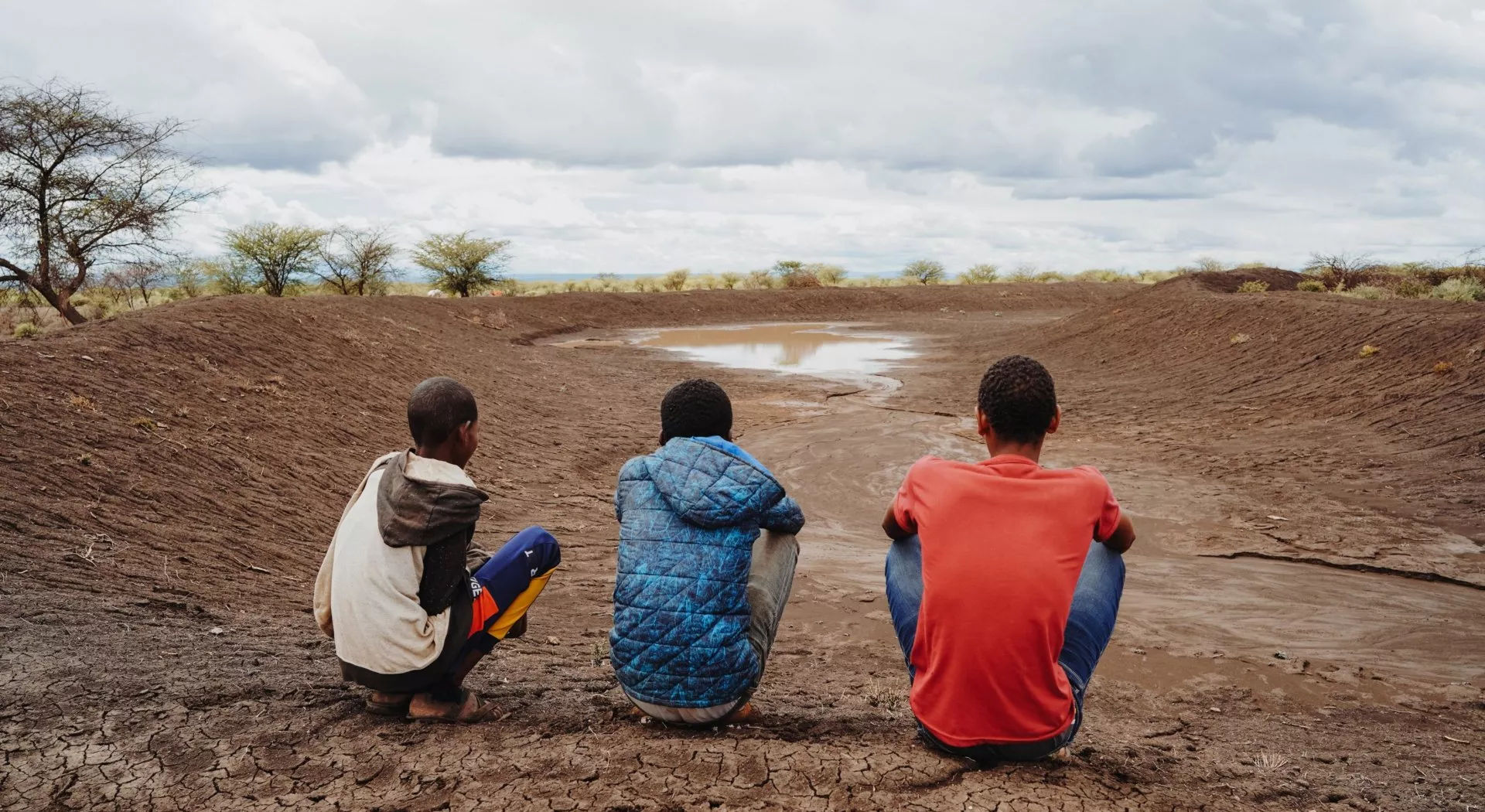 Klimaflüchtlinge: Drei afrikanische Jungs vor einem ausgetrockneten See 