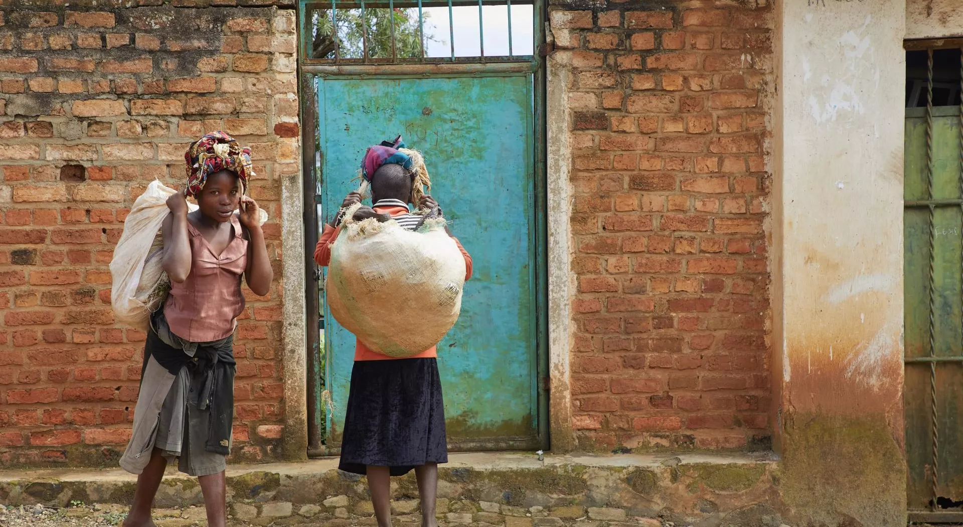 Kongo: Zwei Mädchen mit Säcken voll Nahrung vor ihrer Haustüre