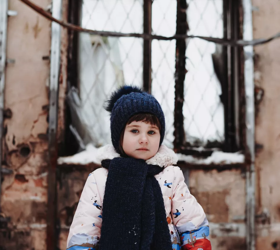Jahresbericht 2022: Ukrainisches Mädchen steht vor zerstörtem Haus im Winter