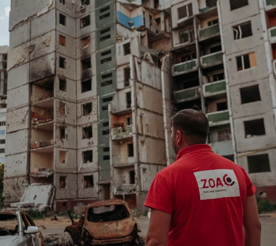 Sicherheit für unsere Mitarbeitenden: Ein ZOA Mitarbeiter steht vor zerstörten Häuser in der Ukraine
