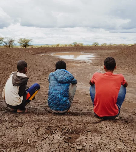 Dürre in Afrika: Drei Jungs sitzen vor einer versiegten Wasserquelle