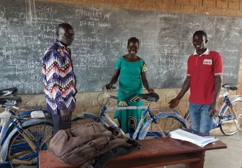 Schulunterricht: Lehrkräfte in Uganda stehen mit ihren Fahrrädern vor der Tafel