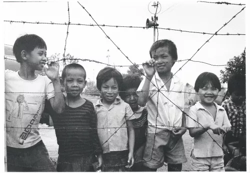 Schwarz-Weiß-Bild zeigt fünf Kinder aus Vietnam an einem Maschendrahtzaun