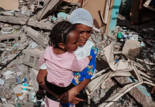 Kampagne für Tigray: Eine Frau steht mit ihrer Tochter auf dem Arm vor den Trümmern ihres Hauses.