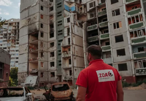 Sicherheit für unsere Mitarbeitender: Ein ZOA Mitarbeiter steht vor zerstörten Häuser in der Ukraine